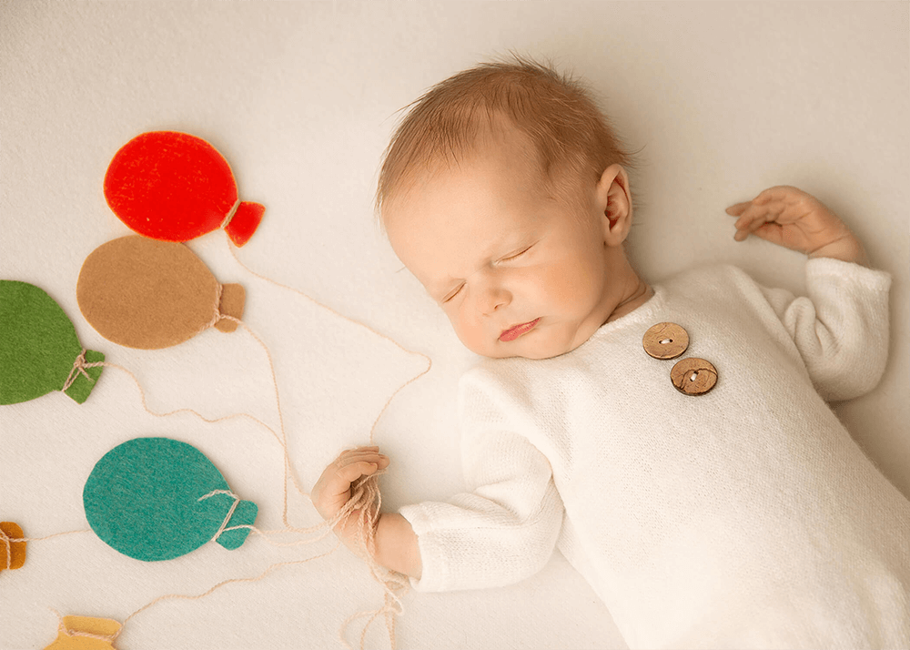 Creative photoshoot of a perfect baby dressed in white holding strings of balloons.