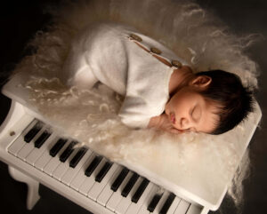 creative baby shoot of a peaceful baby resting on a piano, portraying potential and life for the newborn.